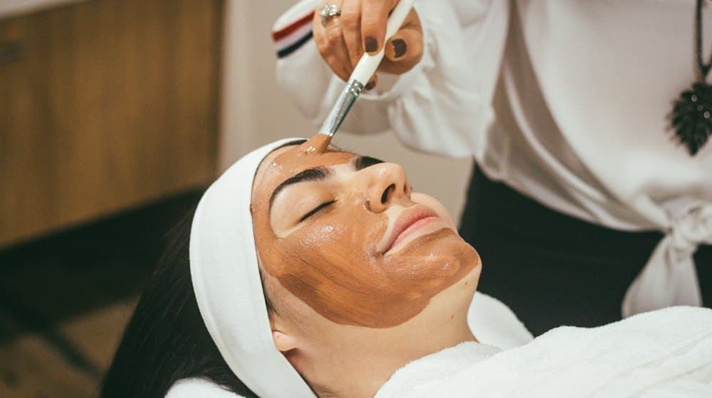 Una esteticista aplicando con pincel una mascarilla de arcilla en un med spa.
