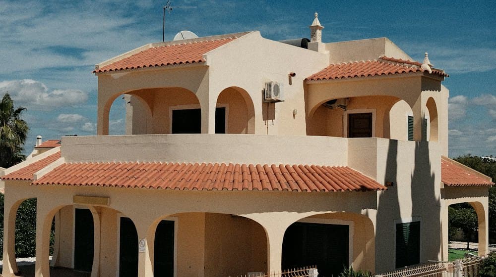 A holiday villa with terracotta roof tiles and arched terraces under a blue sky.