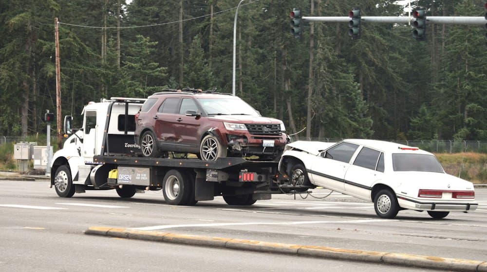 A flatbed tow truck at an intersection, loading a damaged car.
